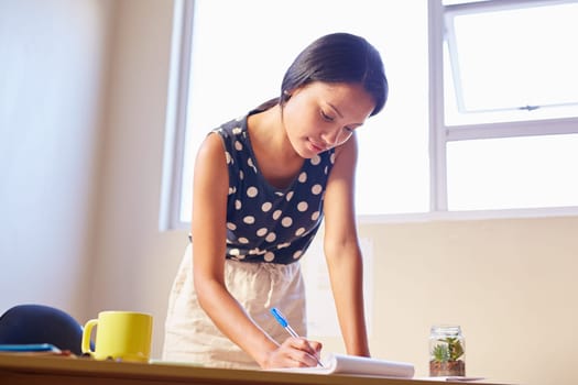 A young woman writing while sitting in her office