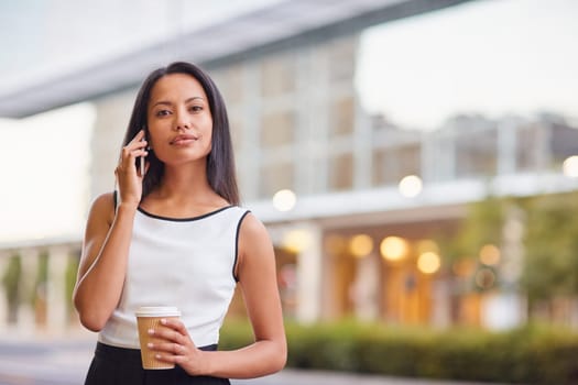 A young businesswoman talking on her phone while standing in front of an office block