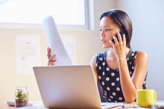 A young businesswoman talking on the phone while looking at a document