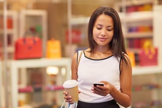 A beautiful young woman sending a text message in a mall