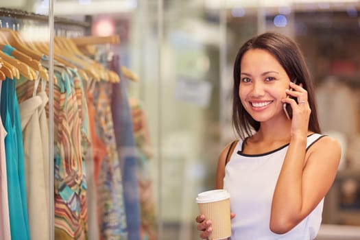 A young woman talking on the phone while browsing for clothes in a shop