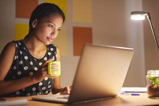 A young woman working on her laptop in her office at night