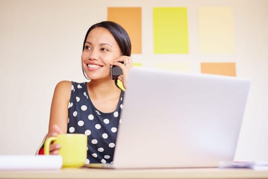 A young businesswoman talking on the phone while sitting in front of her laptop