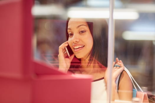 A young woman looking at a handbag through a shop window while talking on the phone