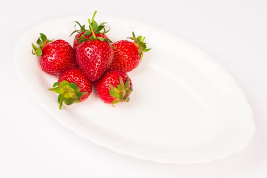 Fresh raw ripe organic strawberries are on white plate on white background.