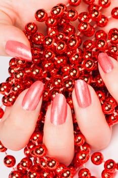 Female hand with light red nails holds red pearls.