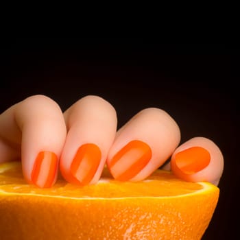 Female hand with orange nails with orange fruit on black background.