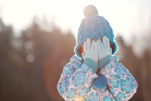 Shot of a little girl in gloves and bobble hat covering her eyes outside on a sunny winter's day