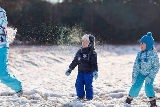 Two kids throwing snowballs at their mother outdoors on a snowy winter's day