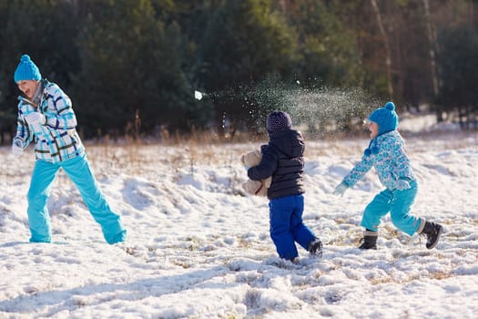 Two kids throwing snowballs at their mother outdoors on a snowy winter's day