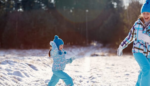 Cute little girl about to throw a snowball at her laughing mother outdoors on a winter's day