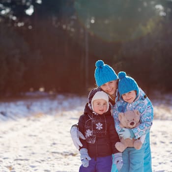 Portrait of a mother and her cute little son and daughter hugging a teddy bear outdoors on a winter's day