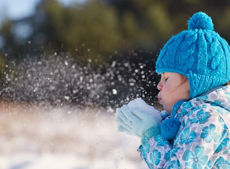 Candid shot of a cute little girl blowing snow flakes from her hands outdoors on a sunny winter's day