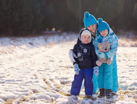 Full length portrait of a mother and her cute little son and daughter hugging a teddy bear outdoors on a winter's day