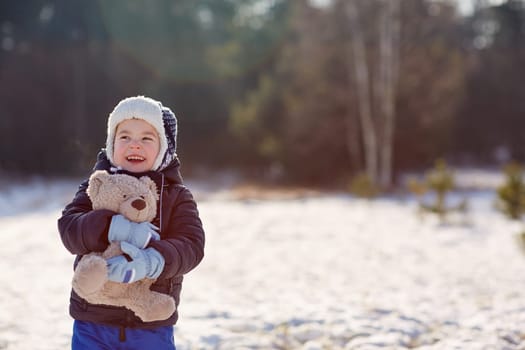 Adorable little boy holding his teddy bear outdoors on a snowy winter's day