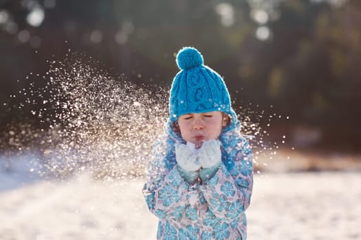 Candid shot of a cute little girl blowing snow flakes from her hands outdoors on a sunny winter's day