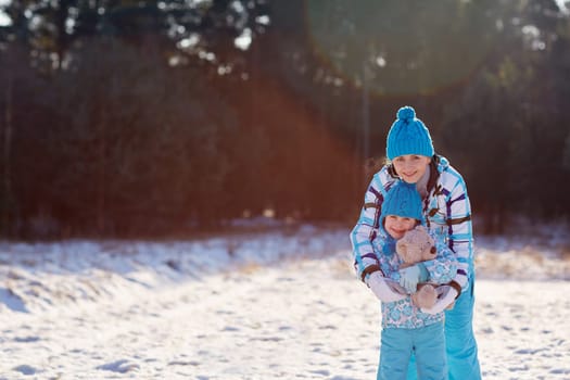 Portrait of a mother and her cute little daughter hugging a teddy bear outdoors on a winter's day