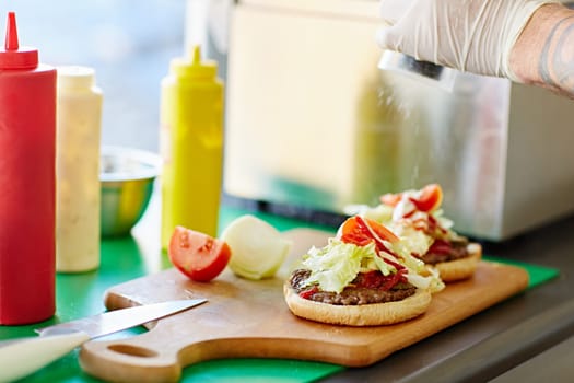 Open hamburger on a wooden board with tomato sauce and mustard dispensers alongside