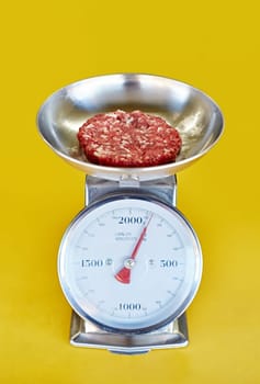 Retro scale against a yellow background with freshly minced red meat in it's bowl being weighed