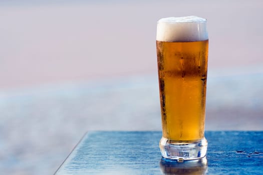 The glass of cold beer is on blue table on gray background.
