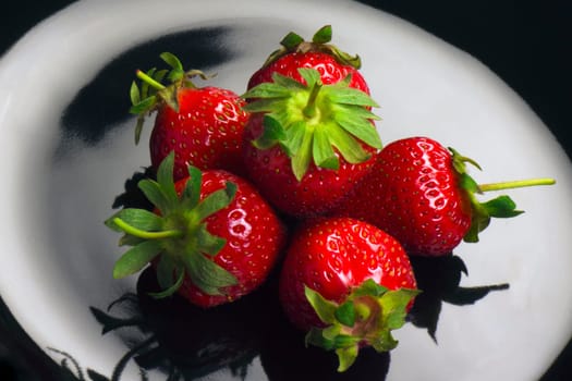 Red ripe fresh strawberries are on black plate.