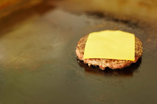 Succulent hamburger patty frying with a slice of fresh cheese melting on top of it