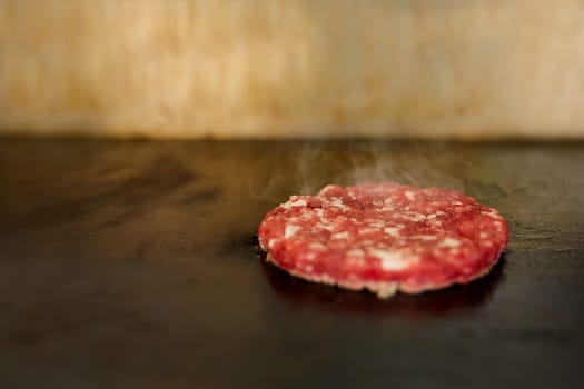 Fresh hamburger patty sizzling on a grill with seasoning on it and steam rising aromatically.