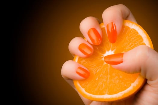 Female hand with orange nails holds an orange fruit.