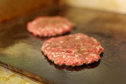 Fresh burger patties seasoning on top frying next to each other on a grill with