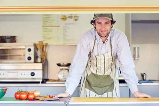 Young male entrepeneur standing confidently in his food stall where he makes and sells takeaway food.