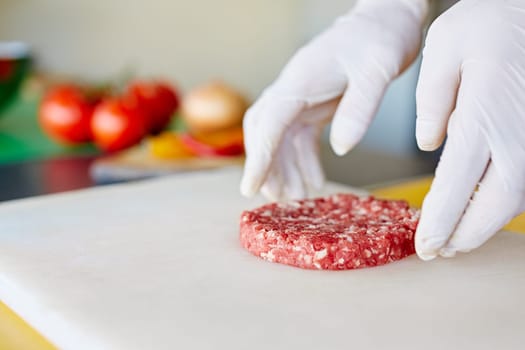Cropped image of hands wearing white latex gloves preparing a hamburger patty in a clean and hygeinic environment.