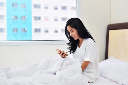 Young asian woman holding smartphone while sitting on the bed