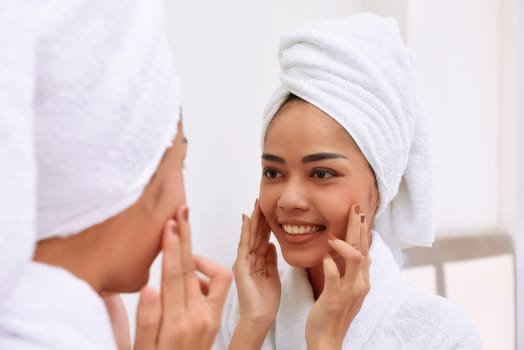 Young asian woman with bath towels cleanses her face at the bathroom