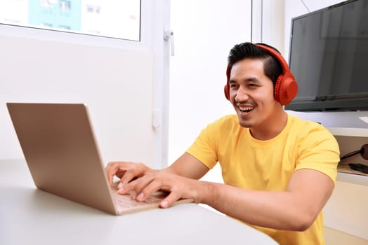 Happy asian man sitting with laptop and headphones in the living room