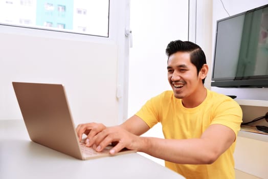 Happy asian man sitting with laptop in the living room