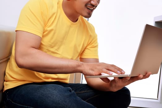 Happy asian man with laptop sitting on the couch at home