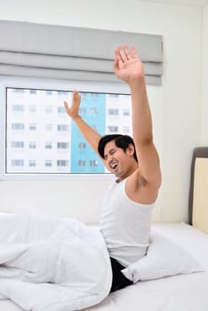 Young asian man waking up and stretching his arms in the morning