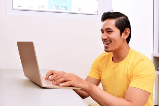 Happy asian man sitting with laptop in the living room