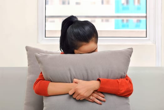 Young asian woman hugging and hiding behind a pillow in the sofa