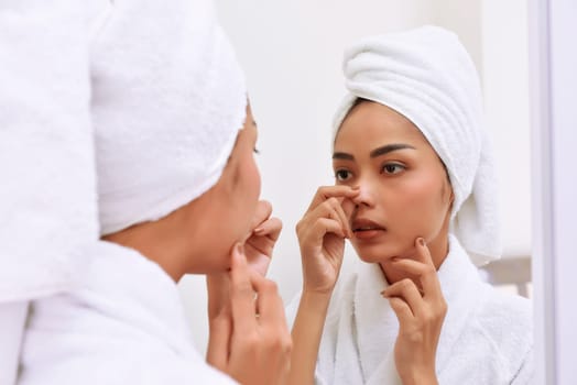 Young asian woman with bath towels cleanses her face at the bathroom