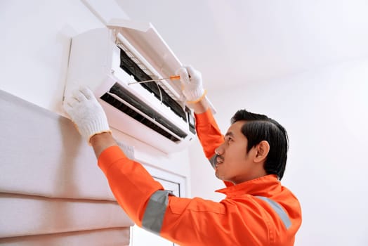 Young asian male technician repairing air conditioner with screwdriver at home
