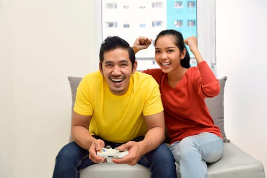 Happy asian couple playing video games and having fun on the living room