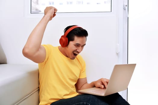 Happy asian man sitting with laptop and headphones in the living room