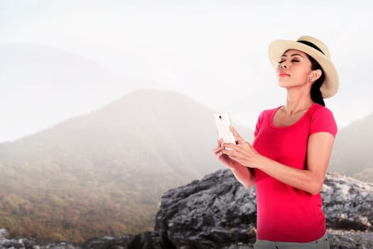 Asian tourist wearing hat holding cellphone at the mountain