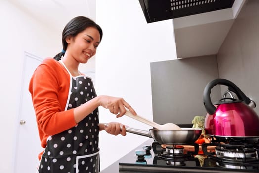 Smiling asian woman using frying pan and cooking in the kitchen