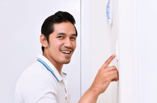 Handsome asian man turning off the light with wall switch in the home