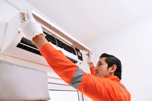 Young asian male technician repairing air conditioner at home