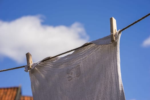 Closeup of white laundry hanging out against the blue sky with old-fashioned wooden clips