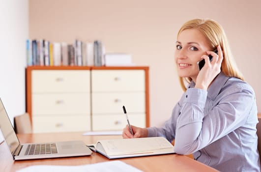 A businesswoman writing something in her diary while sitting in her office