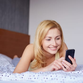 A young woman using her cellphone while lying in bed